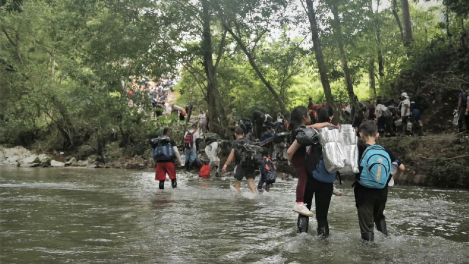 Una mujer cruza un río con sus hijos dentro de la selva del Darién, en Panamá